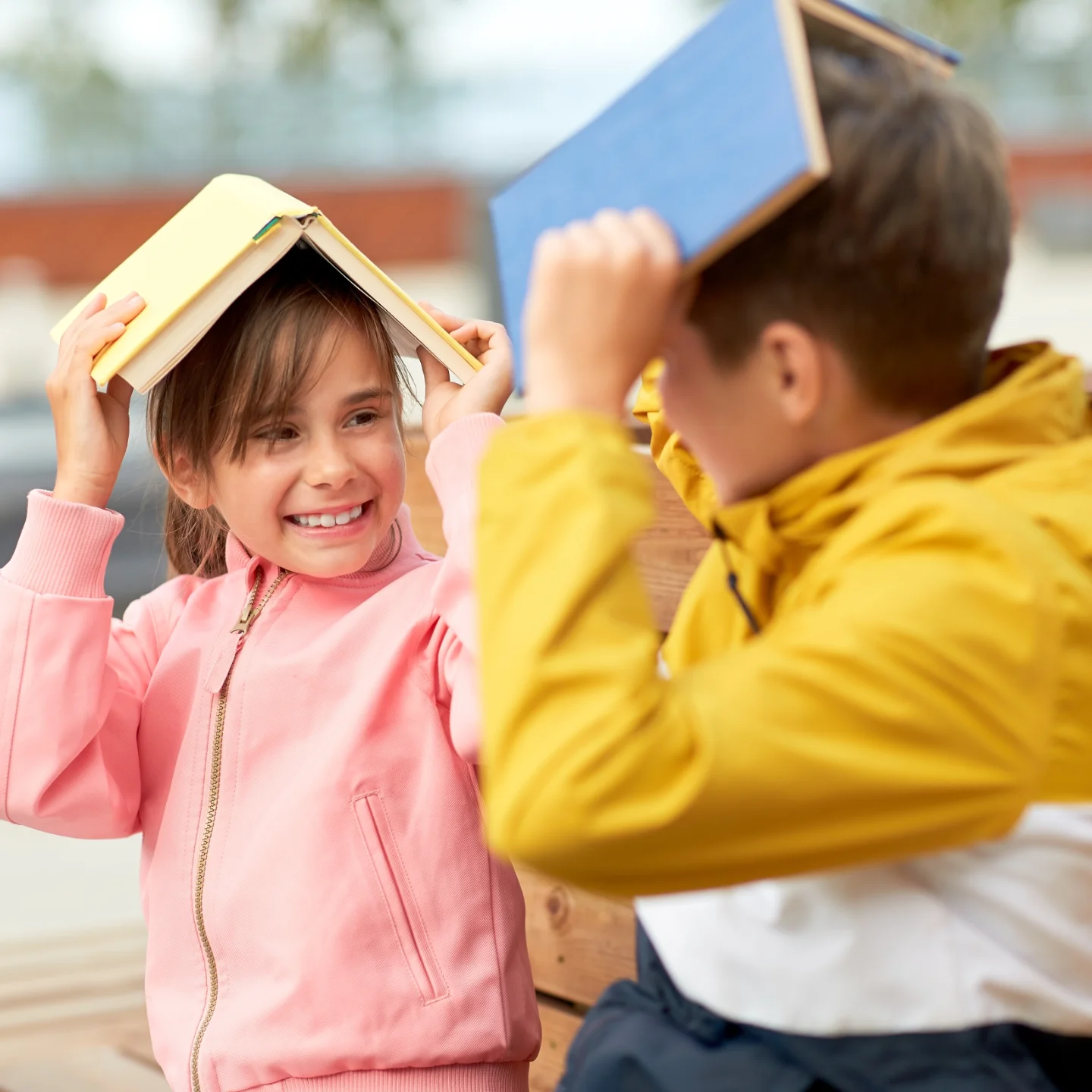 Two young children, a boy and a girl, are playfully balancing a book on their heads.